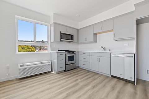 A kitchen with white cabinets and appliances, a window with a view of the outdoors, and a wooden floor.