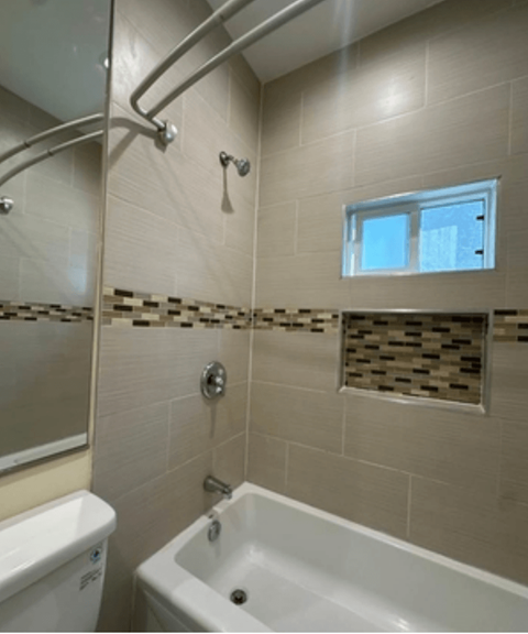 A white bathtub is in a bathroom with a window above it.