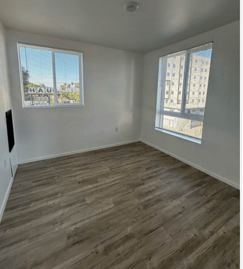 A room with wooden flooring and two windows.