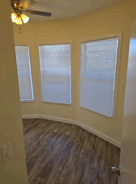 A room with a ceiling fan and three windows.