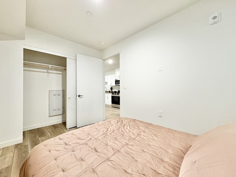 A bedroom with a bed in the foreground and a kitchen in the background.