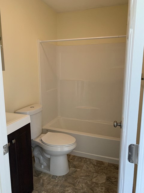 A white toilet sits next to a white bathtub in a bathroom.