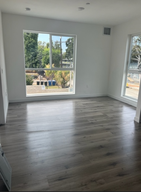 A room with wooden flooring and a large window overlooking a street.