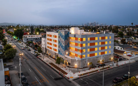 A modern building with orange and blue panels is lit up at dusk.
