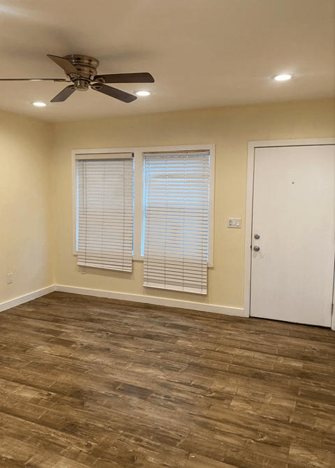 an empty living room with a ceiling fan and two windows