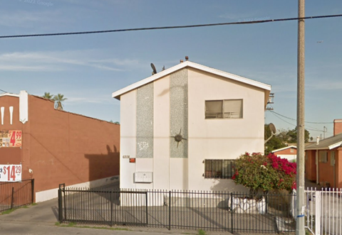 A small house with a white door and a window is surrounded by a black fence.
