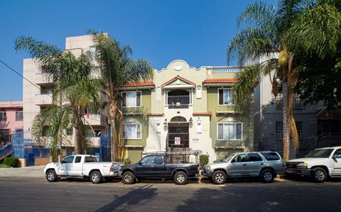 A row of cars are parked in front of a building with palm trees.