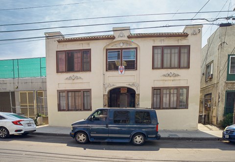 A blue van is parked in front of a two-story building.