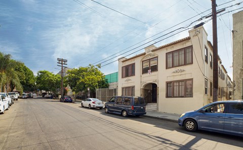 A street view with cars parked on the side of the road and a building with a blue awning in the background.
