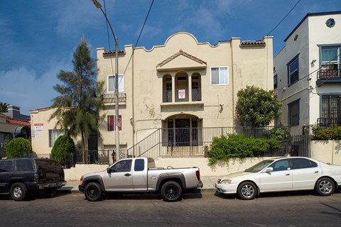 A white pickup truck is parked in front of a tan building.
