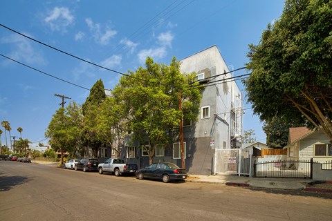 A street with cars parked on the side and a house with a grey facade.