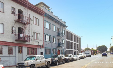 A row of parked cars on a street with buildings on either side.