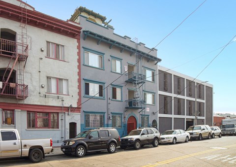 A row of three-story buildings with cars parked in front.