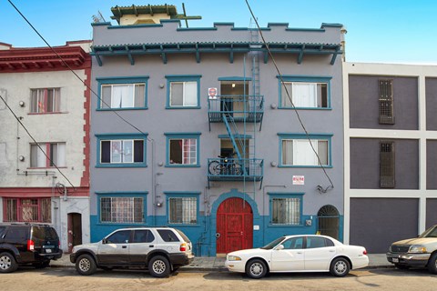 A white car is parked in front of a blue building with a red door.