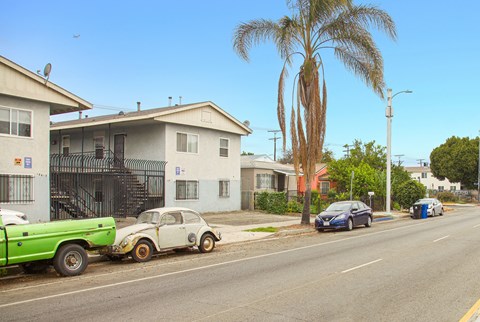 A street with a green truck and a white car with orange rims.