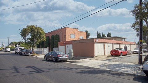 A street view with cars parked on the side and a red car in the driveway.