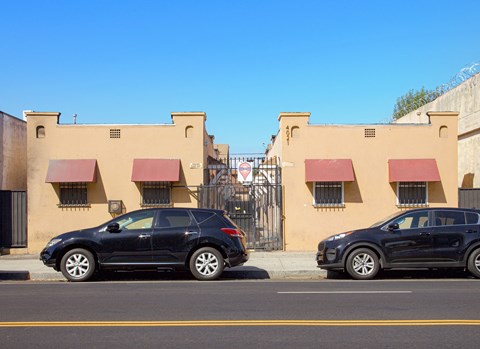 Two black cars are parked in front of a building with red awnings.