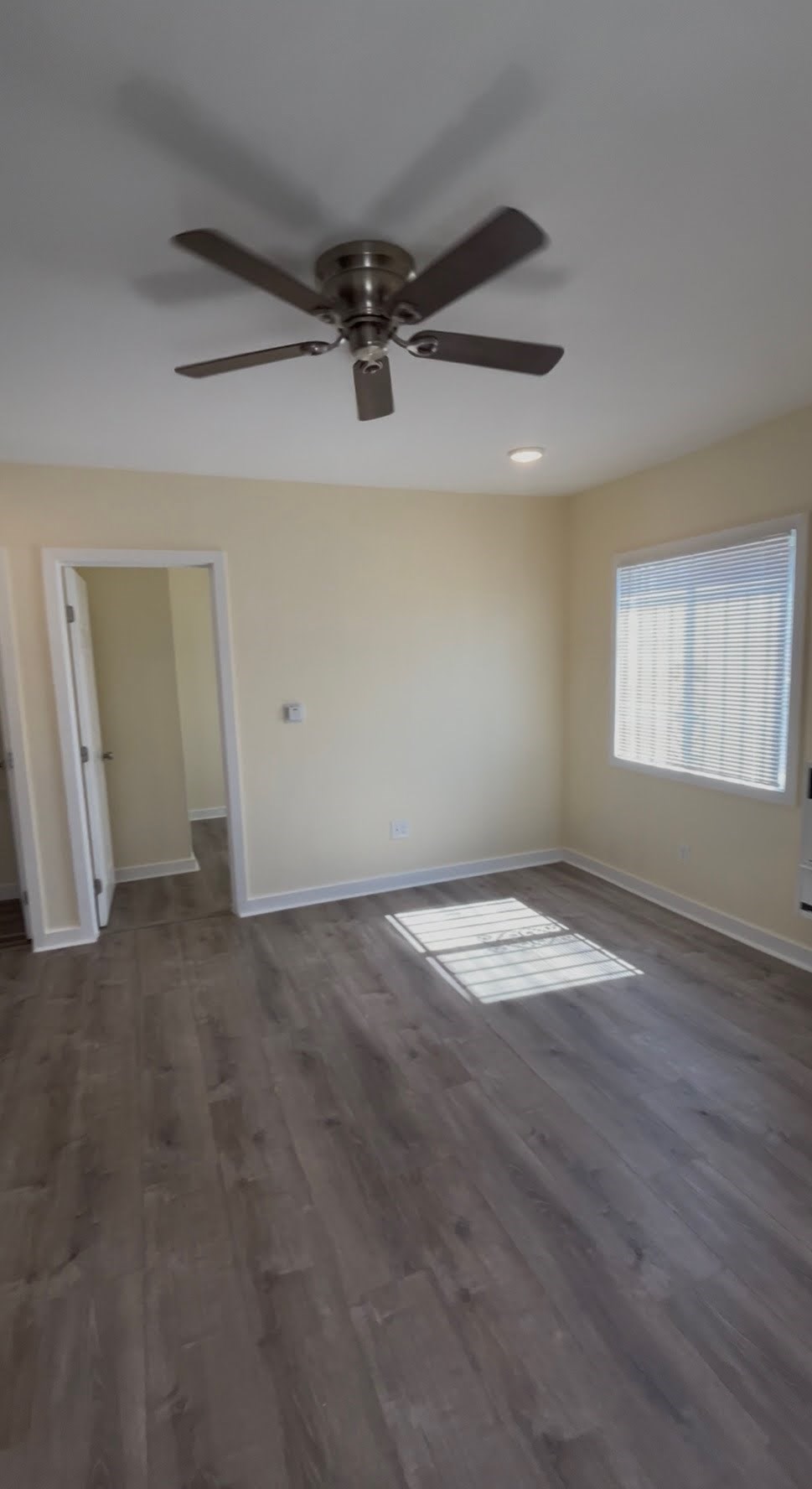 A room with a ceiling fan and a window with blinds.