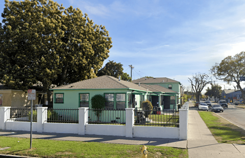 A green house with a white fence in front.