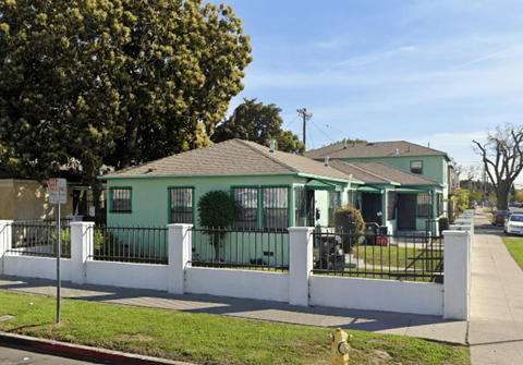A green house with a white fence and a yellow fire hydrant in front.