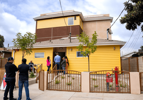 A yellow house with people standing outside.