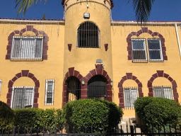 A yellow building with arched windows and a black fence in front.