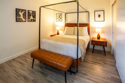 A bedroom with a four poster bed and a bench in front of it.