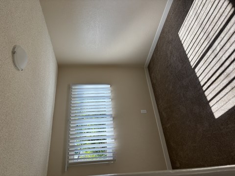 A window with white blinds in a room with a brown wall.