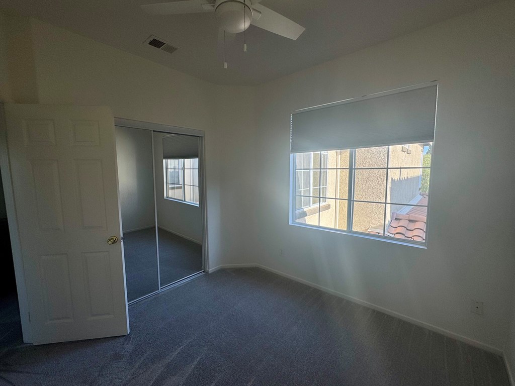 A room with a ceiling fan and a window with blinds.