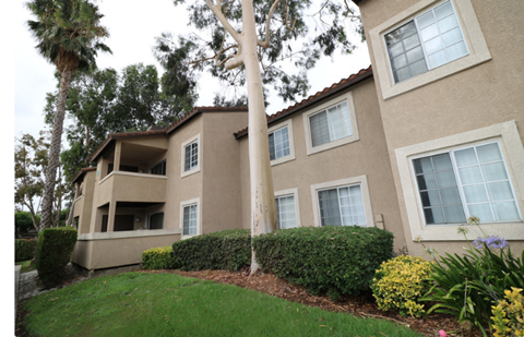 A beige building with a red tile roof and a green lawn in front.