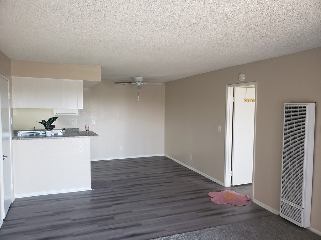 an empty living room with a kitchen in the background