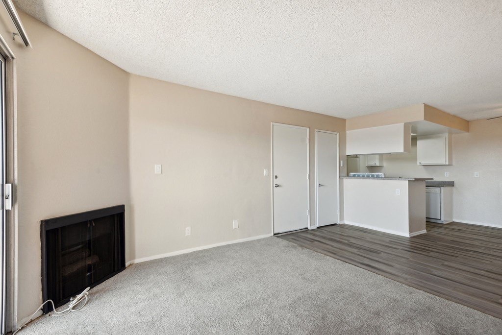 an empty living room with a fireplace and a kitchen