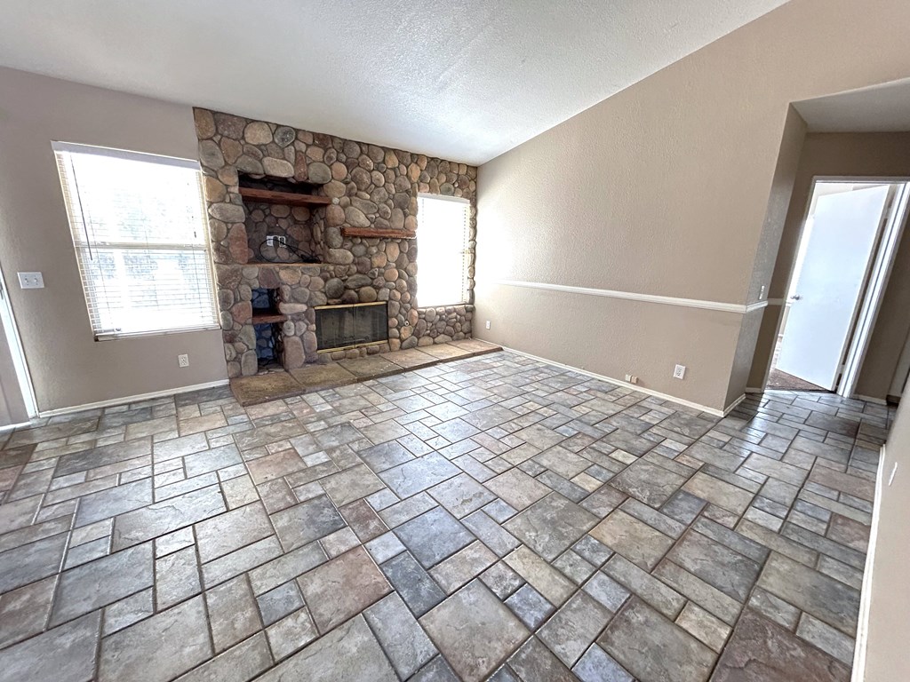 A stone fireplace is in the corner of a room with tile flooring.