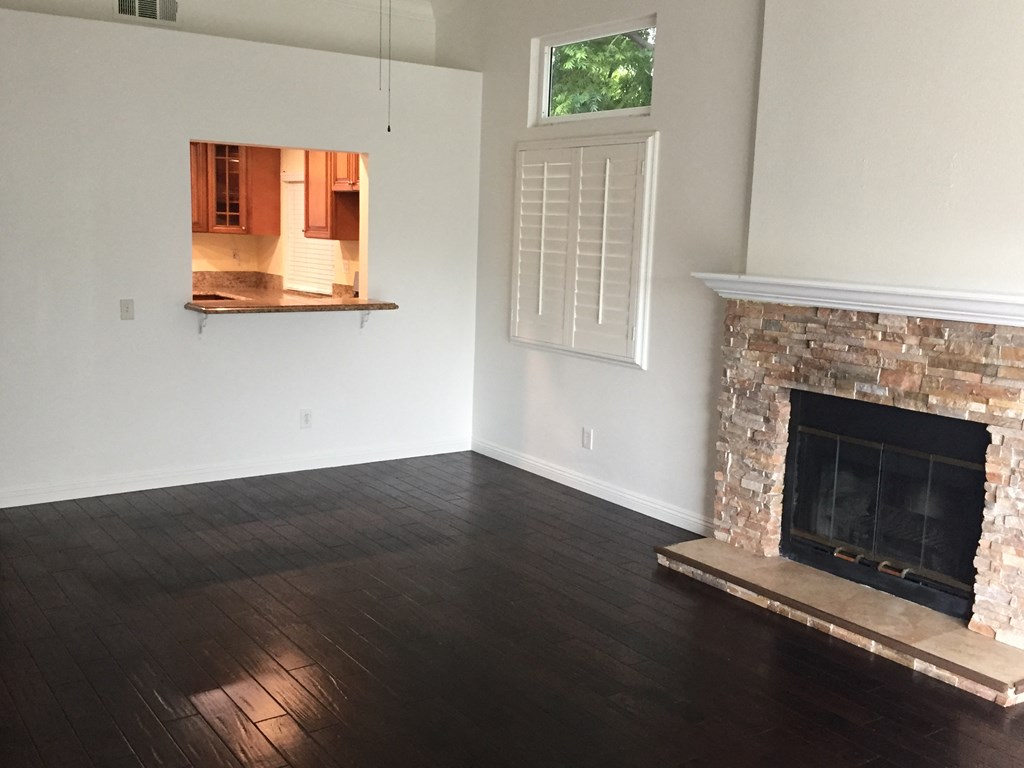 an empty living room with a stone fireplace and hardwood floors
