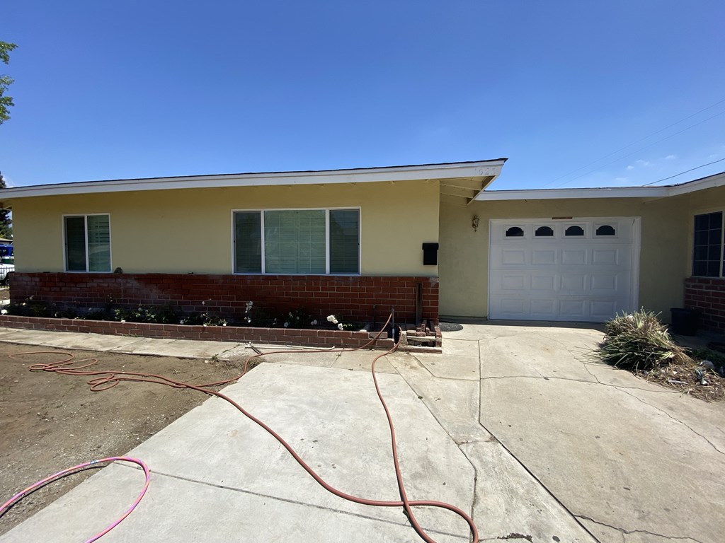 A house with a white garage door and a red hose on the concrete driveway.