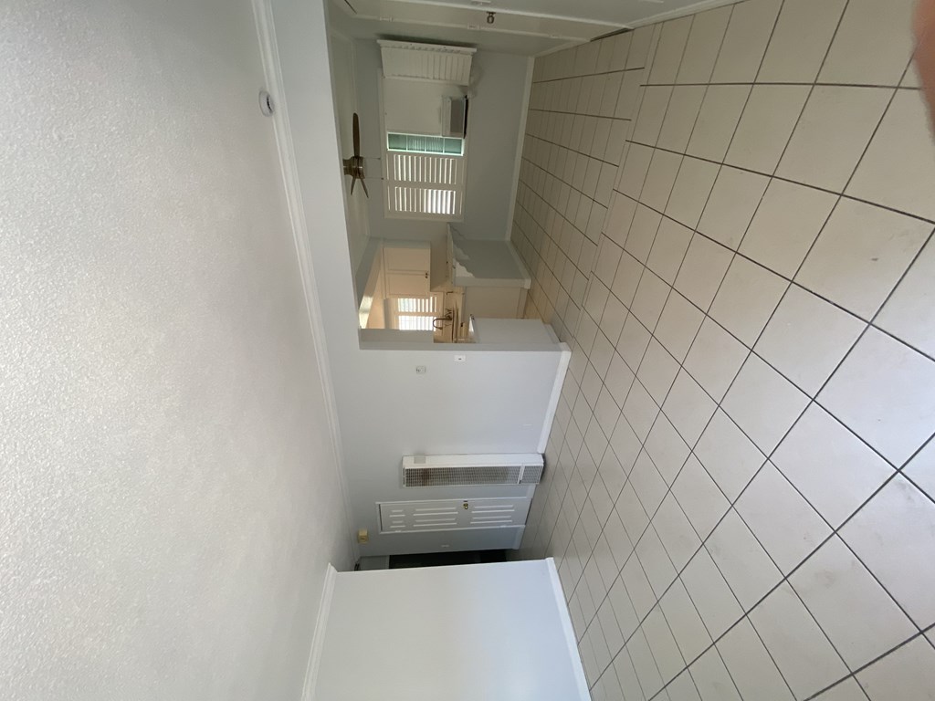A white tiled hallway with a staircase leading to a second floor.
