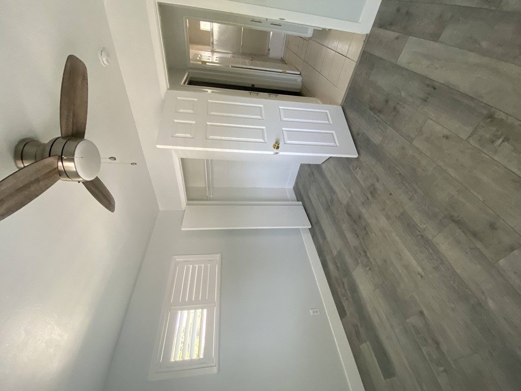 A ceiling fan is mounted on the wall above a window in a room with wood flooring.