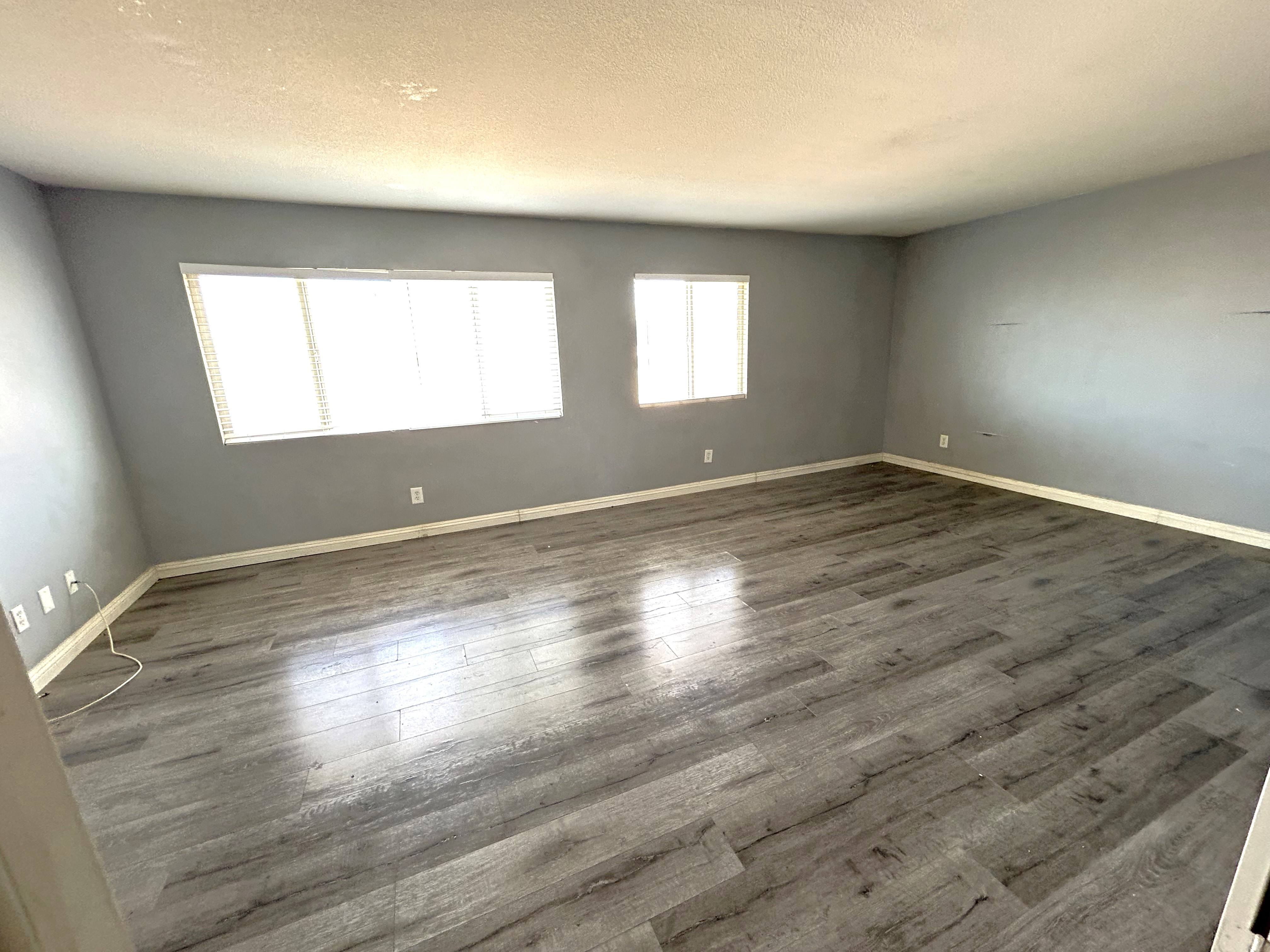 A room with grey flooring and two windows.
