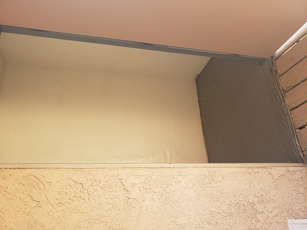 the corner of a room with a beige wall and a window with a silver metal frame