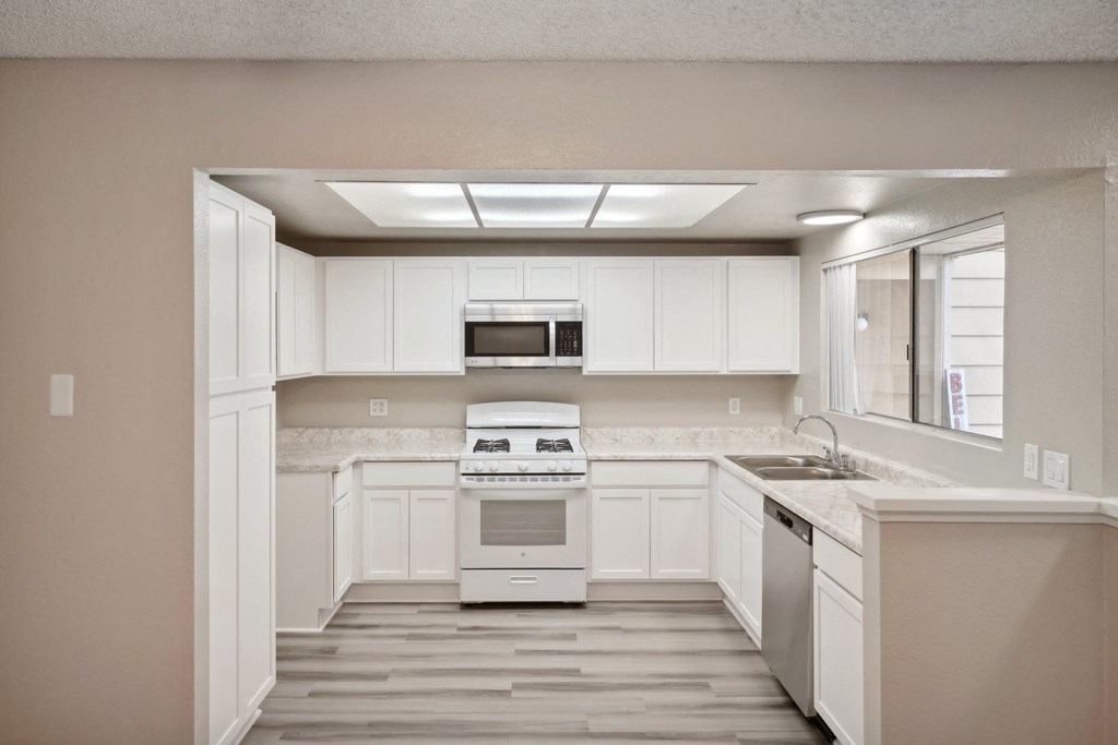an empty kitchen with white cabinets and a window