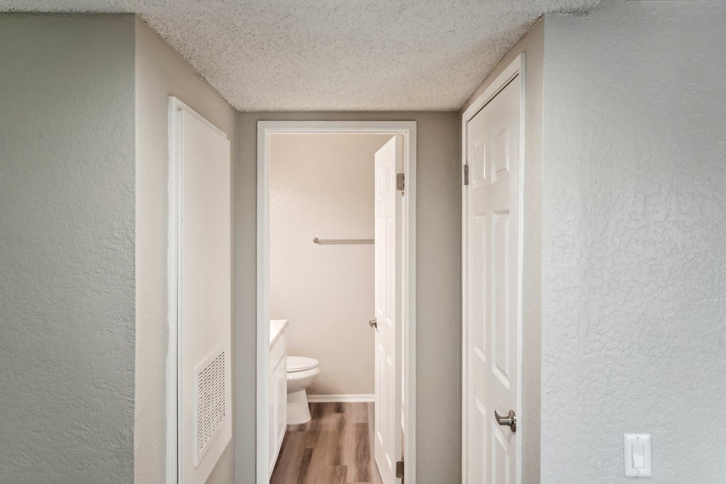an empty hallway with a door open to a bathroom with a toilet