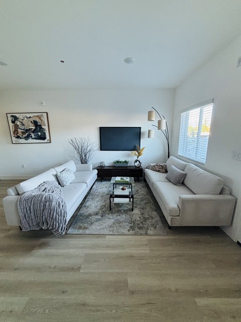 A living room with a white couch, a coffee table, and a flat screen TV mounted on the wall.