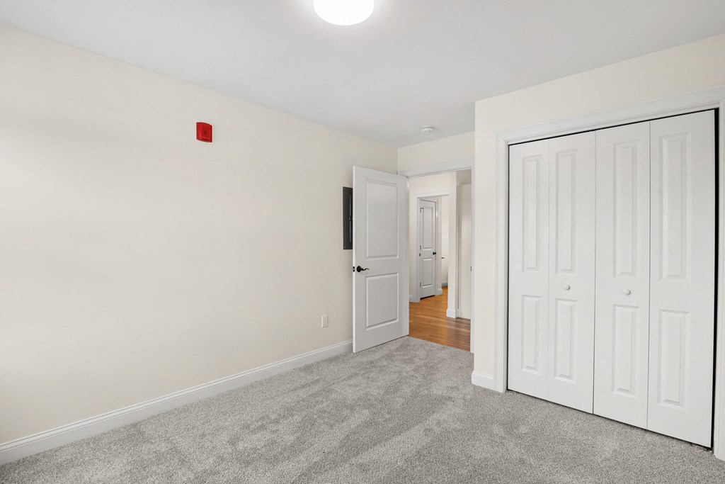 a bedroom with white walls and carpet and a door to a hallway