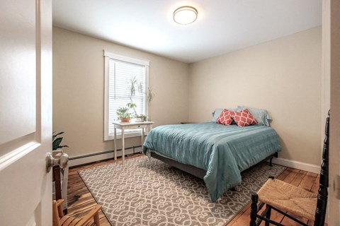 A bedroom with a bed, a chair, and a table with a plant on it.