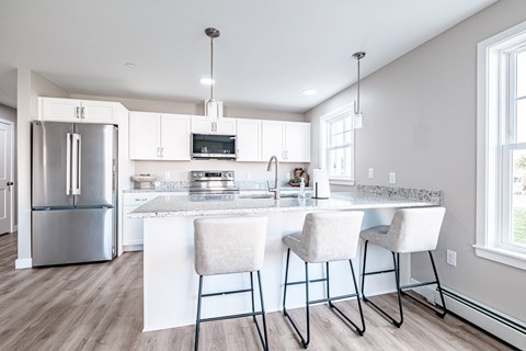 A kitchen with a refrigerator, microwave, and bar stools.
