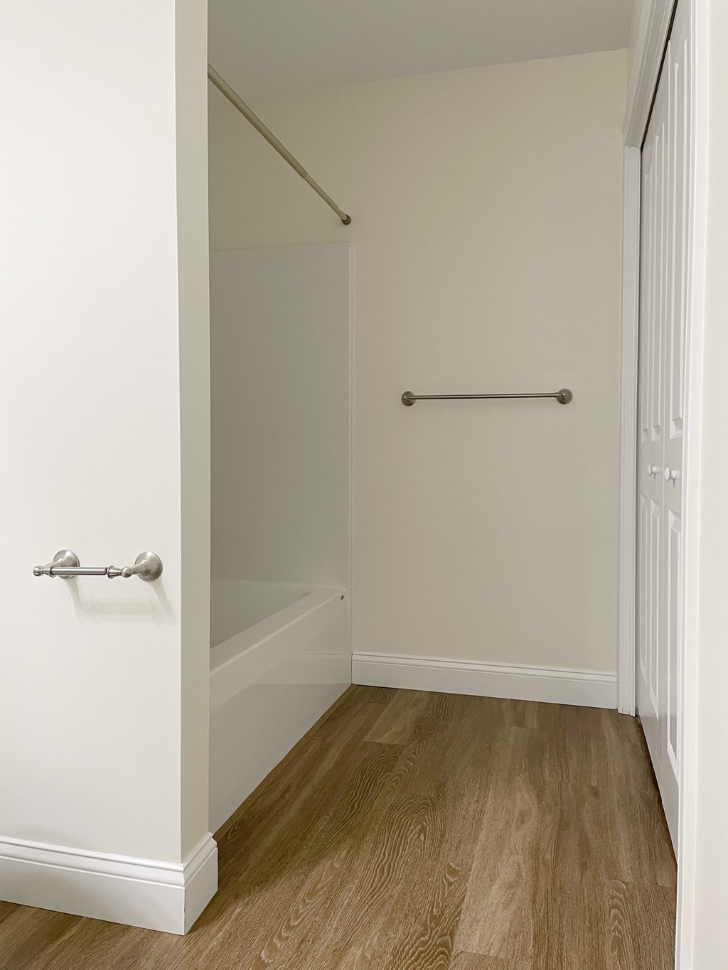 a walk in closet in a home with white walls and wood floors