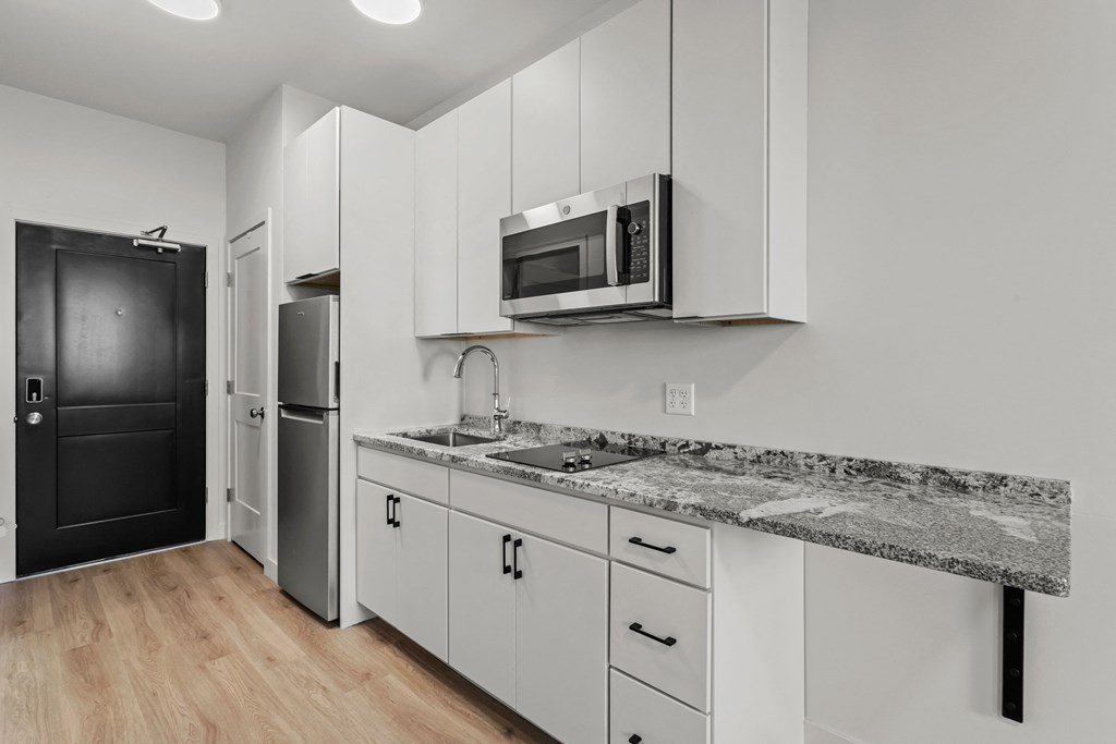 an apartment kitchen with white cabinets and granite counter tops and a black refrigerator and microwave