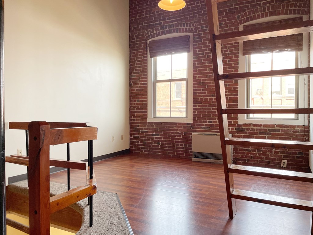 an empty living room with a staircase and a brick wall