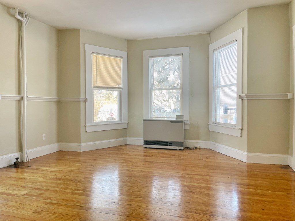 an empty living room with wood floors and three windows
