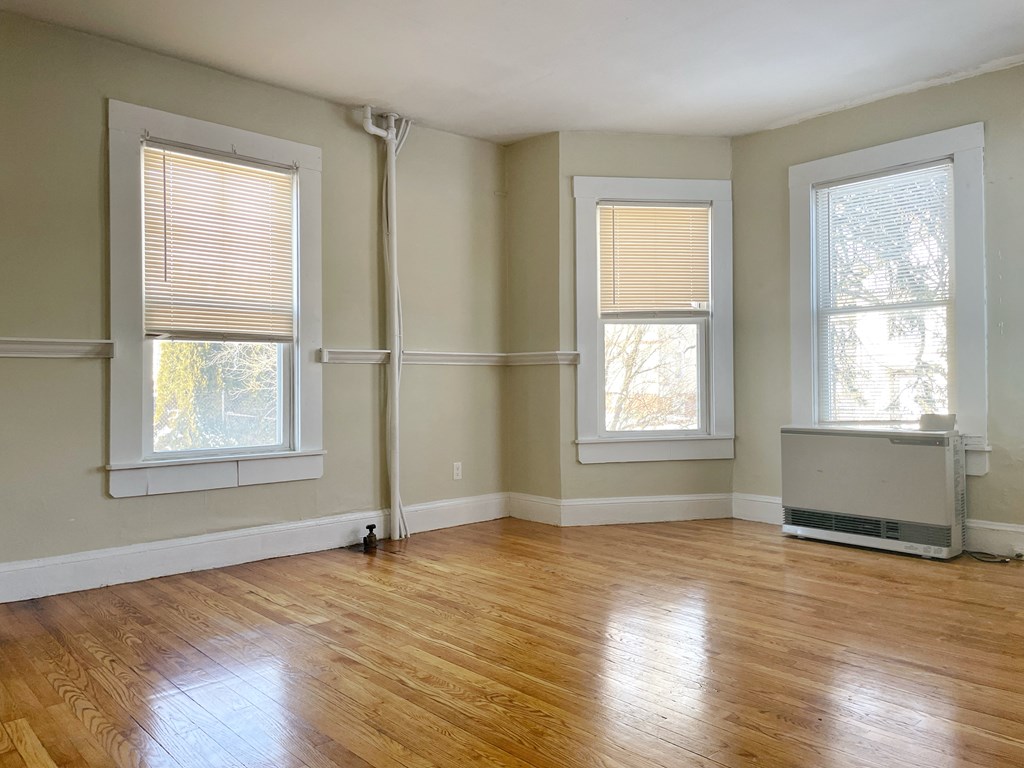 an empty living room with wood floors and three windows